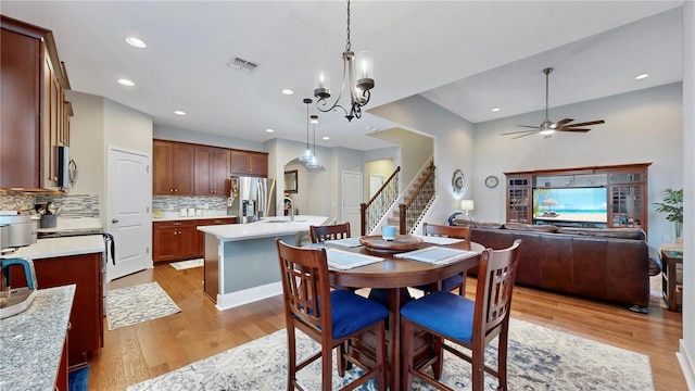 dining area with ceiling fan with notable chandelier, light wood-type flooring, and sink