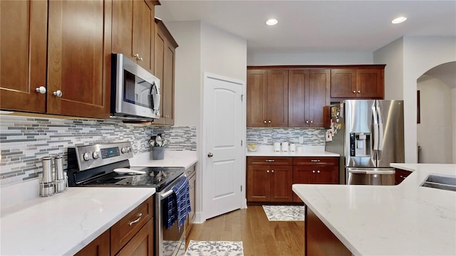 kitchen with light hardwood / wood-style floors, stainless steel appliances, light stone counters, and tasteful backsplash