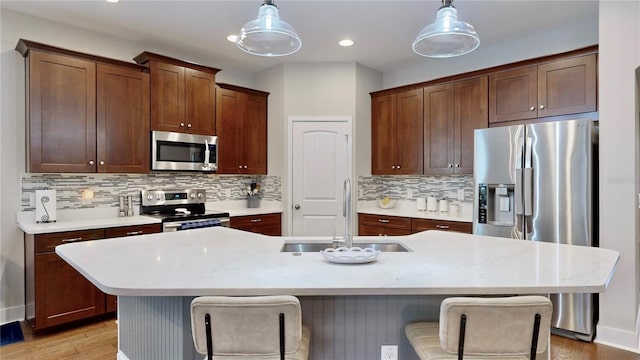 kitchen with appliances with stainless steel finishes, decorative light fixtures, a kitchen island with sink, and sink