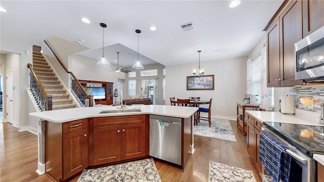 kitchen featuring ceiling fan with notable chandelier, stainless steel appliances, a kitchen island with sink, and decorative light fixtures