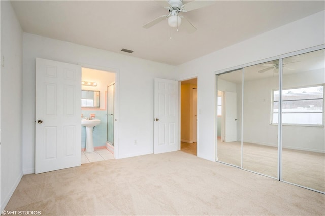 unfurnished bedroom featuring sink, ensuite bath, ceiling fan, light colored carpet, and a closet