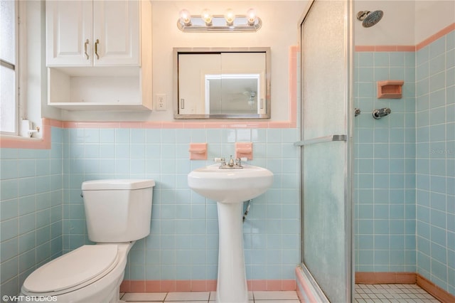 bathroom with tile patterned flooring, a shower with door, toilet, and tile walls