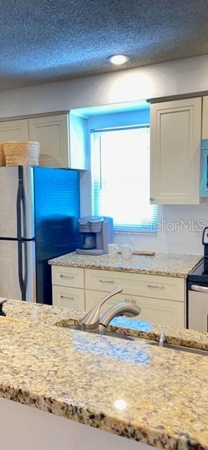 kitchen featuring stainless steel fridge, electric range, white cabinetry, and light stone counters