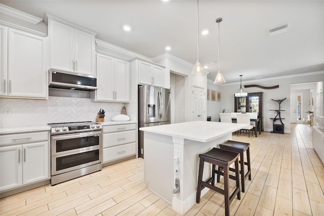 kitchen with decorative light fixtures, a kitchen island, stainless steel appliances, decorative backsplash, and white cabinets