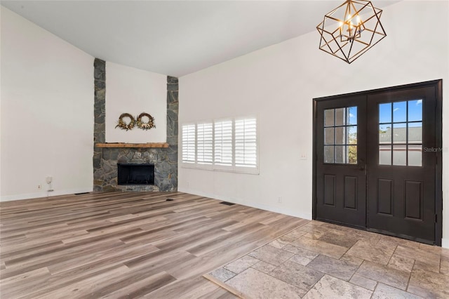 entryway with light hardwood / wood-style flooring, an inviting chandelier, a high ceiling, a stone fireplace, and french doors