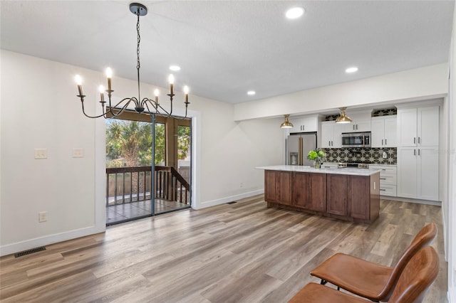 kitchen with pendant lighting, white cabinetry, stainless steel appliances, a center island with sink, and decorative backsplash