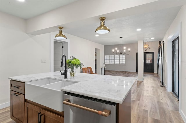 kitchen with sink, light stone counters, light wood-type flooring, stainless steel dishwasher, and an island with sink