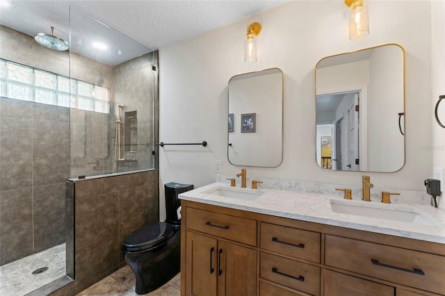 bathroom with tile patterned flooring, a tile shower, vanity, a textured ceiling, and toilet