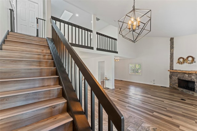 staircase featuring a towering ceiling, wood-type flooring, a fireplace, and a notable chandelier