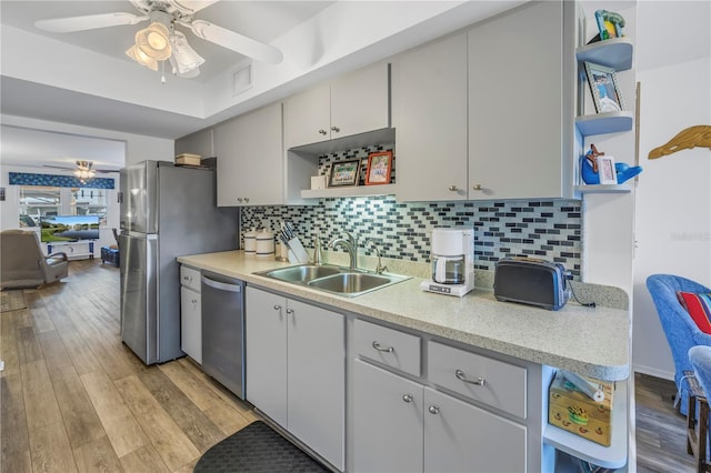 kitchen with appliances with stainless steel finishes, backsplash, ceiling fan, sink, and light hardwood / wood-style flooring