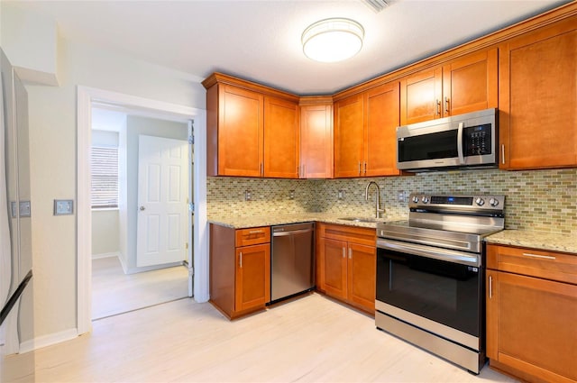 kitchen featuring sink, light stone counters, light wood-type flooring, appliances with stainless steel finishes, and decorative backsplash