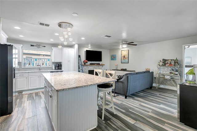 kitchen with hanging light fixtures, ceiling fan, stainless steel fridge, a kitchen island, and white cabinetry