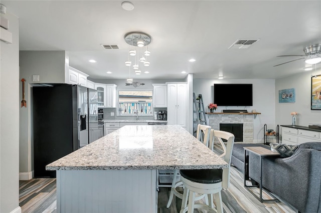 kitchen featuring a fireplace, ceiling fan, decorative light fixtures, light hardwood / wood-style flooring, and white cabinets