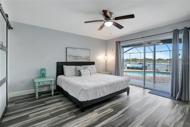 bedroom featuring ceiling fan, a barn door, dark hardwood / wood-style flooring, access to outside, and a water view