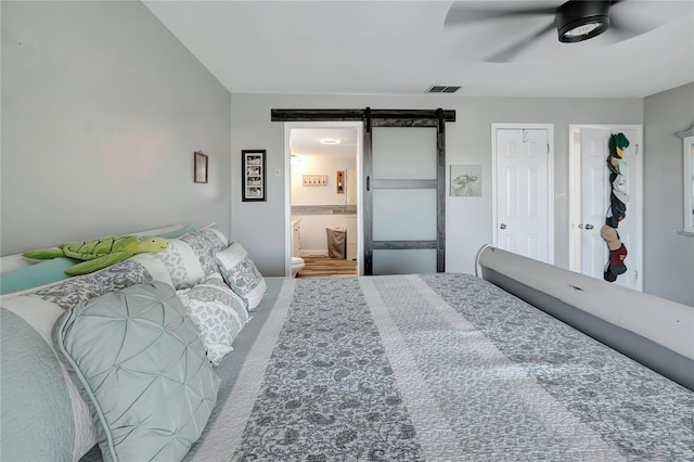 bedroom featuring a barn door, ceiling fan, and ensuite bath