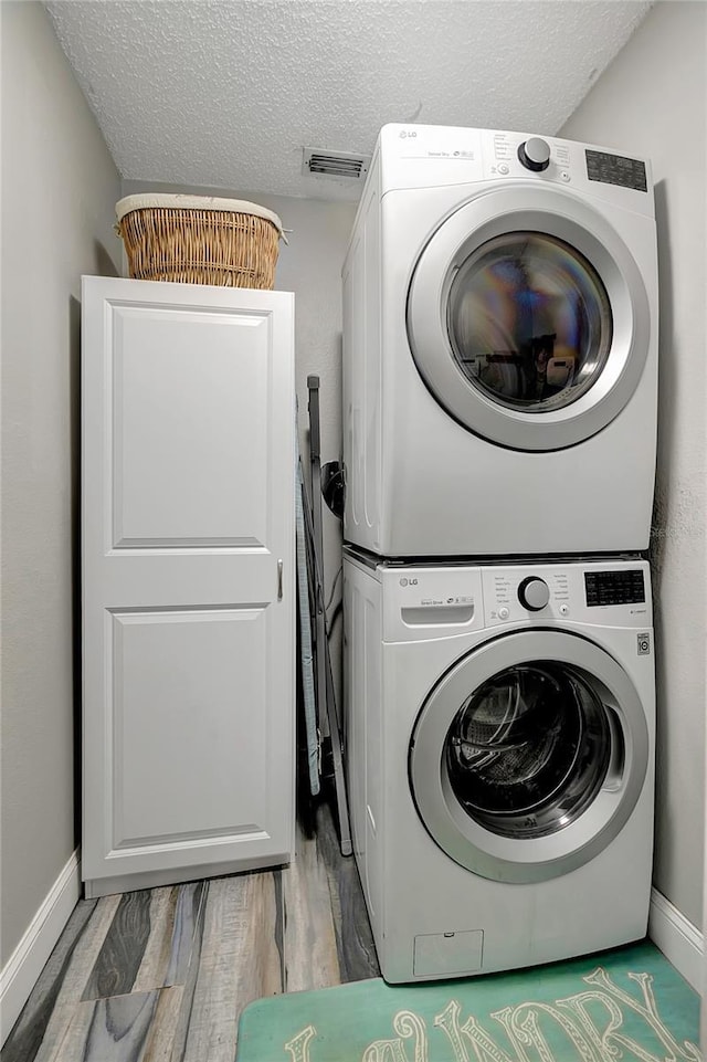 washroom featuring a textured ceiling, stacked washer and dryer, and hardwood / wood-style flooring