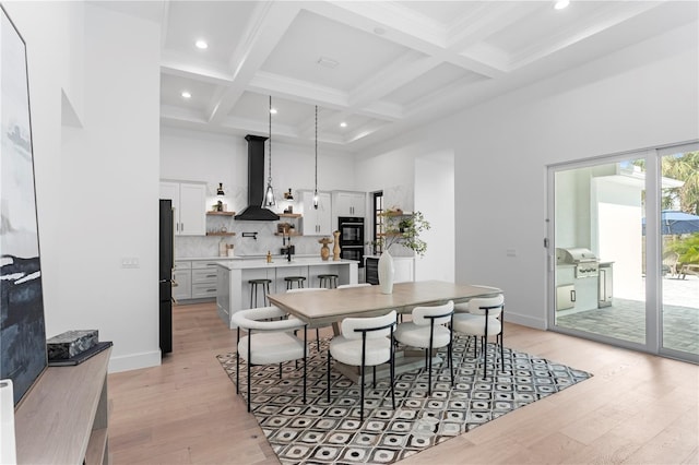 dining space with beam ceiling, light wood-type flooring, a towering ceiling, and coffered ceiling