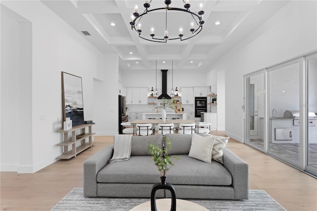 living room featuring coffered ceiling, light wood-type flooring, a towering ceiling, beamed ceiling, and a chandelier