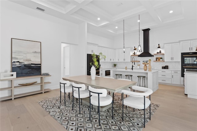 dining space with sink, coffered ceiling, beamed ceiling, a towering ceiling, and light wood-type flooring