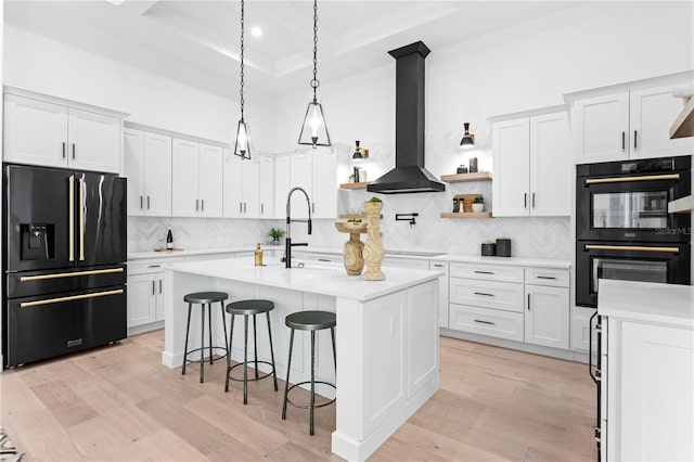 kitchen with white cabinetry, wall chimney range hood, tasteful backsplash, an island with sink, and black appliances