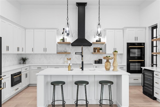 kitchen with an island with sink, white cabinetry, beverage cooler, and black appliances