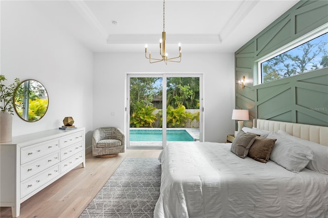 bedroom with access to exterior, a notable chandelier, light hardwood / wood-style floors, a tray ceiling, and ornamental molding