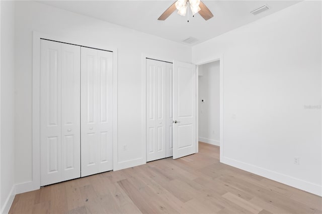 unfurnished bedroom featuring ceiling fan, light hardwood / wood-style flooring, and multiple closets