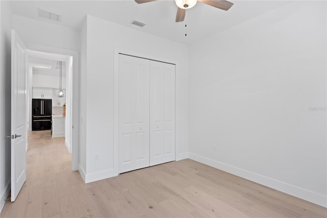 unfurnished bedroom with light hardwood / wood-style floors, a closet, high end black refrigerator, and ceiling fan