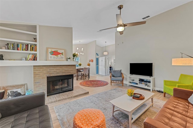 living room with built in shelves, lofted ceiling, a fireplace, ceiling fan with notable chandelier, and light wood-type flooring