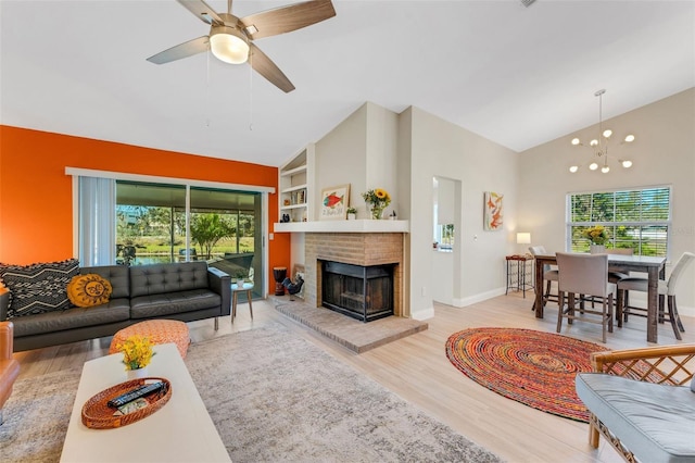 living room with built in shelves, a fireplace, ceiling fan with notable chandelier, and light wood-type flooring