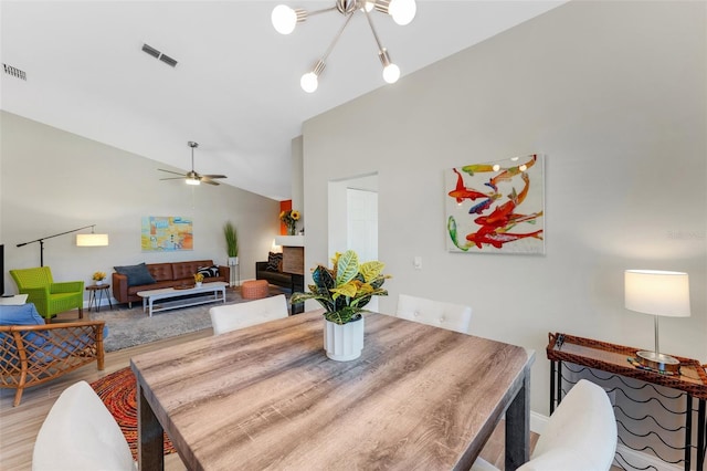 dining space with a brick fireplace, lofted ceiling, ceiling fan with notable chandelier, and hardwood / wood-style flooring