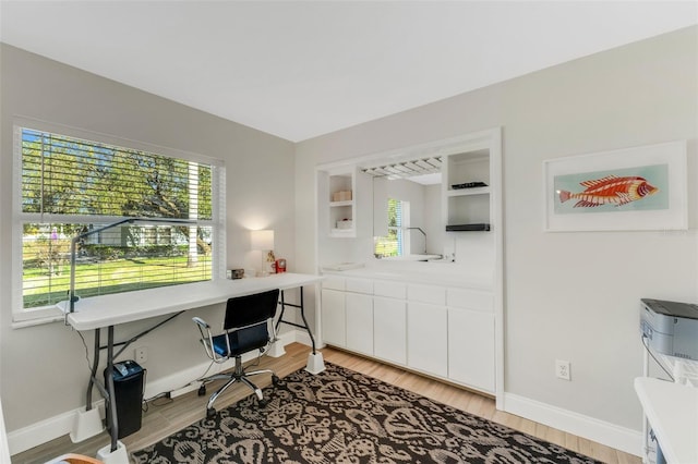 office space with built in shelves and light hardwood / wood-style flooring