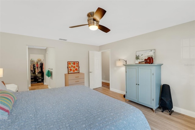 bedroom featuring a walk in closet, a closet, light hardwood / wood-style flooring, and ceiling fan