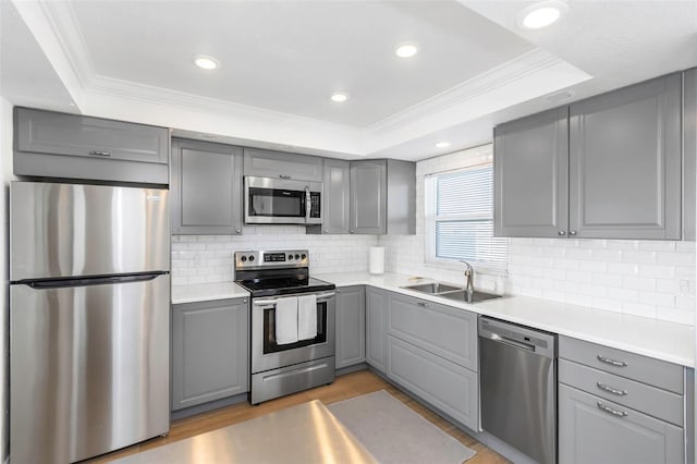 kitchen with gray cabinetry, sink, decorative backsplash, appliances with stainless steel finishes, and a tray ceiling