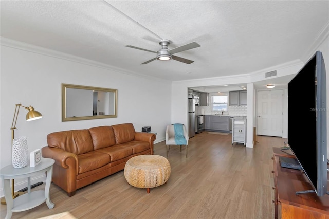 living room featuring sink, ceiling fan, ornamental molding, a textured ceiling, and light wood-type flooring