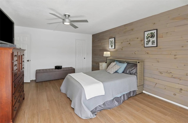 bedroom featuring ceiling fan, wood walls, and light wood-type flooring