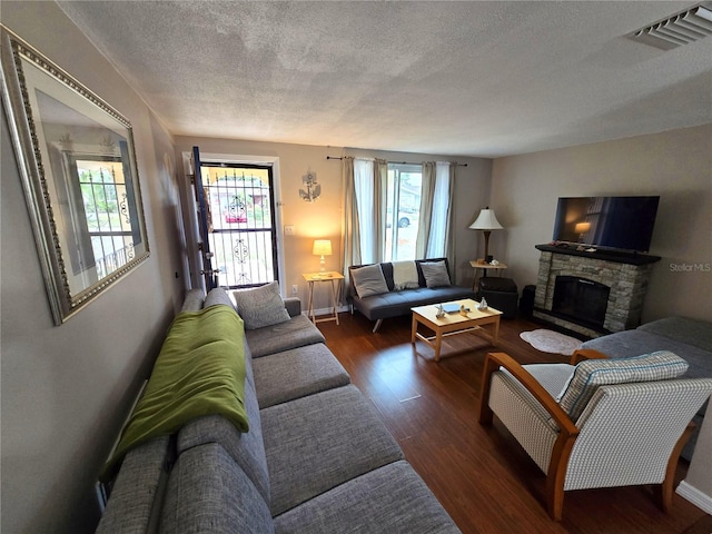 living room featuring a stone fireplace, dark wood-type flooring, a healthy amount of sunlight, and a textured ceiling