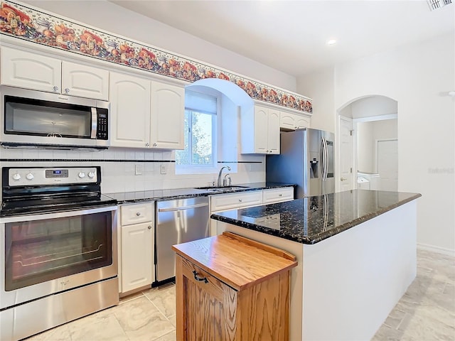 kitchen with sink, dark stone countertops, a kitchen island, white cabinetry, and stainless steel appliances