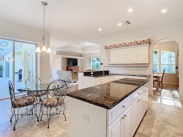 kitchen with dark stone counters, ceiling fan, decorative light fixtures, white cabinets, and a center island