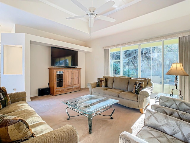 living room with a raised ceiling, light colored carpet, and ceiling fan