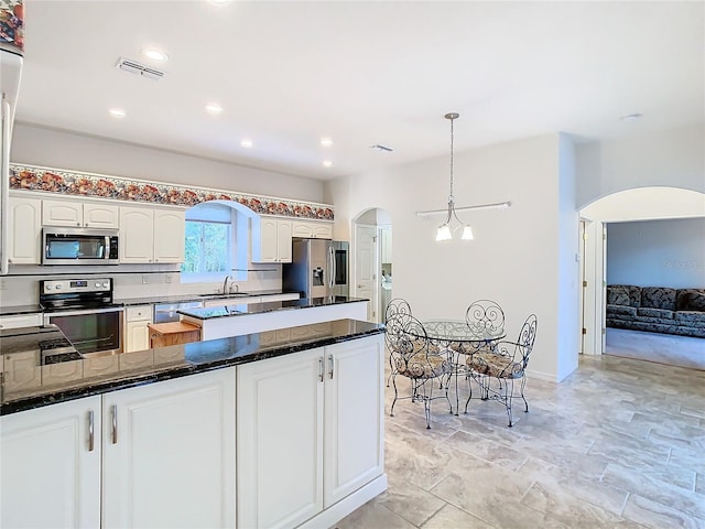 kitchen featuring pendant lighting, dark stone countertops, arched walkways, stainless steel appliances, and a sink