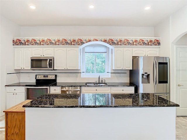 kitchen with appliances with stainless steel finishes, white cabinetry, dark stone counters, and a sink