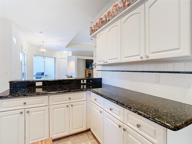 kitchen with white cabinets, backsplash, kitchen peninsula, and dark stone countertops