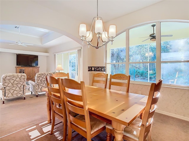 carpeted dining room with a raised ceiling, plenty of natural light, ceiling fan with notable chandelier, and arched walkways