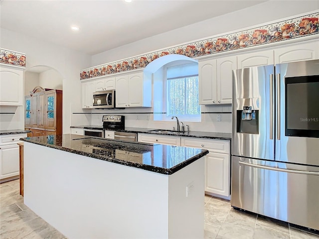 kitchen featuring dark stone countertops, stainless steel appliances, arched walkways, white cabinetry, and a sink