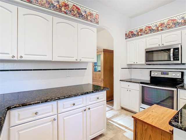 kitchen with dark stone counters, white cabinets, arched walkways, and stainless steel appliances