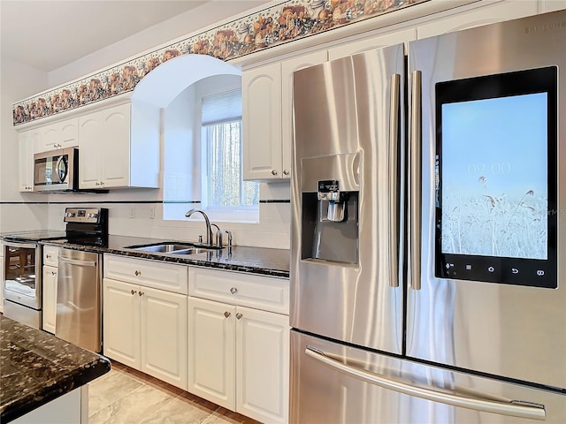 kitchen with tasteful backsplash, dark stone countertops, stainless steel appliances, white cabinetry, and a sink