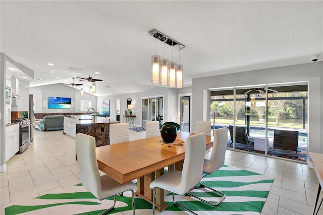 dining space with ceiling fan with notable chandelier, a textured ceiling, sink, lofted ceiling, and light tile patterned flooring