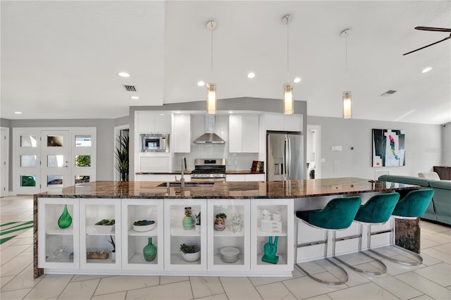 kitchen featuring white cabinetry, sink, wall chimney range hood, decorative light fixtures, and appliances with stainless steel finishes