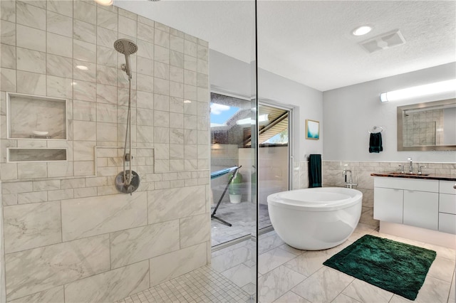 bathroom with plus walk in shower, vanity, a textured ceiling, and tile walls